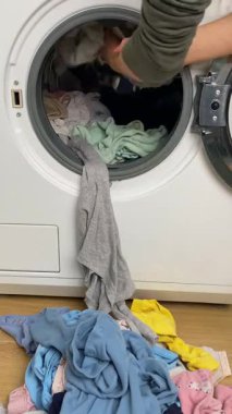 Kadın ev işleri yapıyor çocukları renkli kirli çamaşırlarla çamaşır makinesine yüklüyor. Kirli çamaşırları varil temizleme konsepti dikey videosuna yükler. Yüksek kalite 4k görüntü