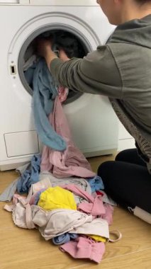 Ev işi yapan bir kadının dikey videosu, renkli çocukların kirli çamaşırlarını çamaşır makinesine yüklüyor. Ev temizliği, çamaşır rutini ve günlük ev işleri kavramı. Yüksek kalite 4k görüntü