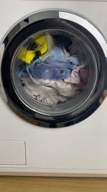 Ön yükleme makinesi, varilin içindeki renkli çamaşırlarla çalışmaya başlıyor. Yıkama döngüsü sırasında parlak kıyafetlerin devrilmesi, ev işleri konsepti, temizlik. Yüksek kalite 4k görüntü