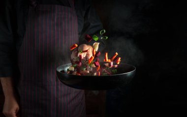 Şef kızartma tavasında sebze hazırlar. Sağlıklı vejetaryen yemekleri ve yemekleri karanlık bir arka planda pişirmek. Ücretsiz reklam alanı