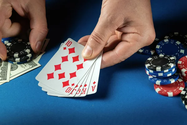 The player bets on a winning combination royal flush in poker game on a blue table with chips and money in a club.