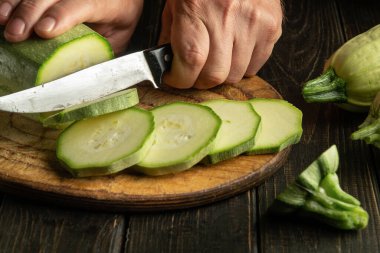 Bıçaklı bir aşçı vejetaryen yemeği hazırlamadan önce tahta kesme tahtasıyla sebze iliği kesiyor.