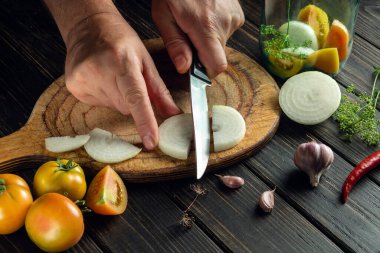 Aşçı mutfak kesme tahtasındaki bir bıçakla soğanı keser. Kavanozda muhafaza etmek için köylü ürünleri