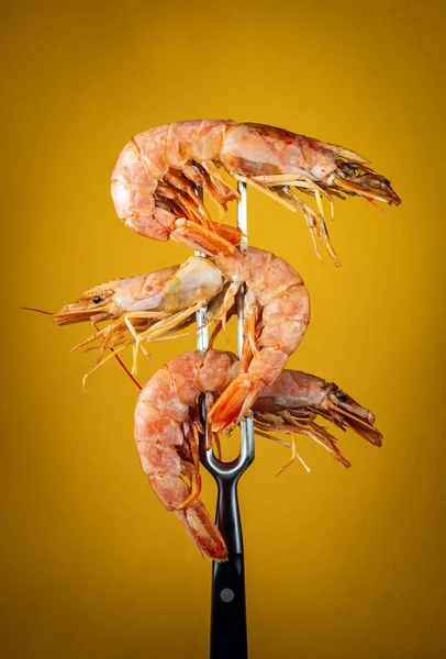 Three boiled tiger prawns or king shrimps on a fork. Delicious food idea for hotel or restaurant on yellow background.