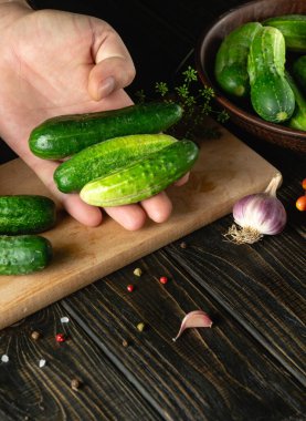 The cook sorts cucumbers before canning in a jar. Work environment on kitchen table with vegetables and spices.