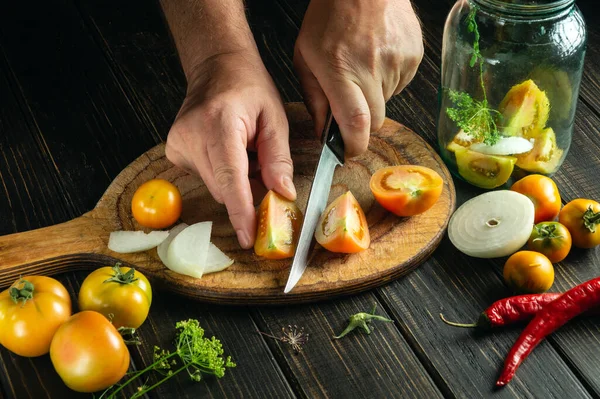 stock image The cook hands cuts a tomato on a kitchen cutting board. Peasant food for preparing preserves in a jar