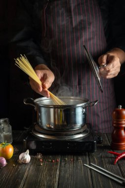 Profesyonel şef mutfakta sıcak bir tencerede organik makarna hazırlıyor. Lezzetli otel yemeği tarifi