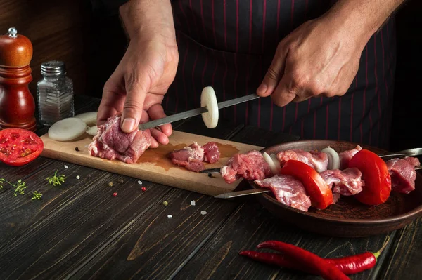 Professional chef prepares shish kebab with raw lamb meat and onions. Punching meat on a skewer by the hands of a cook