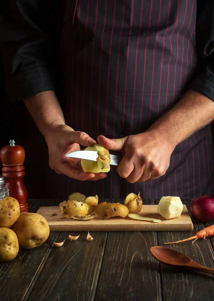 The cook peels potatoes for cooking French fries. Working environment in the kitchen of a restaurant or cafe