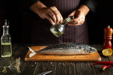 Aşçı otel mutfağındaki uskumru balığına yağ ekler. Scomber lezzetli yemek pişirmede en iyisidir.