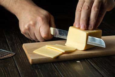 Aşçı elinde bıçakla sandviç, italyan pizzası ya da mutfakta atıştırmak için tahta tahtada peynir kesiyor. Yemek hazırlığı. Sağlıklı beslenme ve yaşam tarzı. Yiyecek konsepti