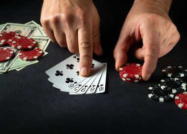 Pokerde kazanan floş kombinasyonuna parmağıyla puan veren oyuncu siyah bir masada çipler ve kumarhanede para ile birlikte.