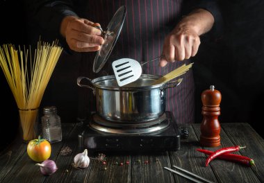 Profesyonel şef sebzeli bir tencerede makarna pişirir. Lokanta ya da otel için lezzetli bir yemek tarifi.