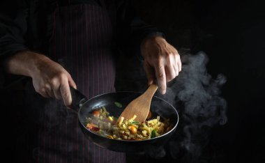 Şefin elinde sıcak tavada baharatlı taze sebze ve makarna pişirmek. Siyah arkaplanda tarif veya menü için boşluk