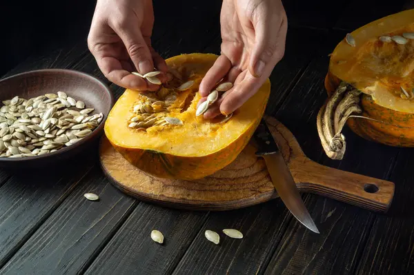 stock image The chef takes out the seeds from the pumpkin for use in cooking. Peasant food on a black background