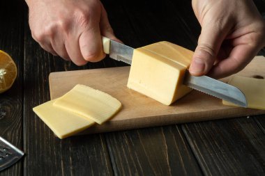 Bir restoranın mutfağında, peynir dilimleyen bıçaklı bir aşçı elinin yakın çekimi. Diyetteyken kahvaltı için süt ürünleri hazırlıyorum.