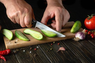 The cook cuts fresh cucumbers for pickling with spices and vegetables. Close-up of a chef hands while working on a kitchen table in a restaurant.