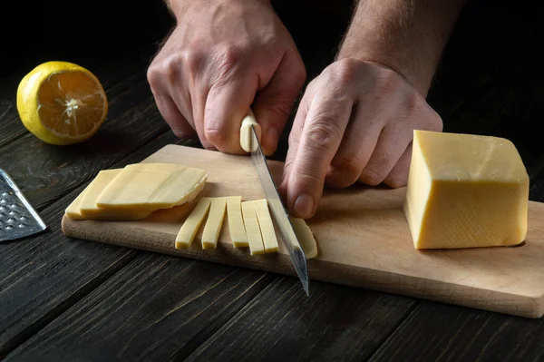 The hands of the chef with a knife cut the cheese into small pieces for tasting. Delicious Milk Cheese Recipe Presentation.