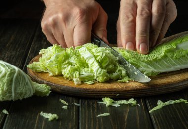 Bir şefin eli, vejetaryen yemeği hazırlamak için kesme tahtasına yeşil yapraklı marul kesiyor. Esmer arka planda lezzetli kahvaltı konsepti