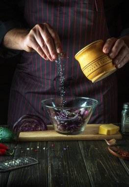 Şef, restoranın mutfağında taze kırmızı lahana salatasına tuz serpiyor. Sağlıklı ya da vejetaryen yemekleri pişirmek