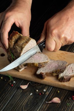 Aşçı pişirilmiş bifteği bıçakla mutfak kesme tahtasının üzerinde bıçakla keser. Bir otel ya da restoran için yemek pişirme kavramı. Reklam veya tarif için koyu arkaplan