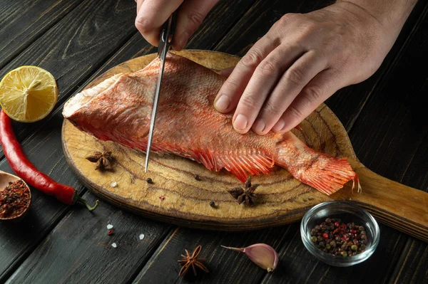 The chef cuts raw Sebastes fish on a kitchen cutting board. Delicious red fish dinner for restaurant or hotel.