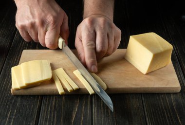 Bıçaklı bir şefin elleriyle kesme tahtasındaki peyniri dilimlemek. Lokanta mutfağında lezzetli bir öğle yemeği için süt ürünleri pişiriyorum..