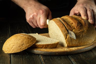 Aşçı elinde bıçakla mutfak tahtasındaki ekmeği keser. Pastanedeki sağlıklı yiyecek kavramı..