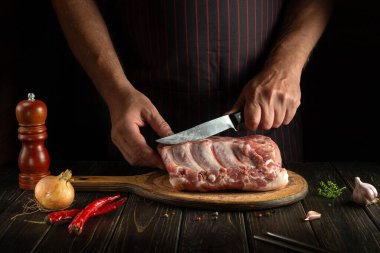 Aşçı ızgara ya da barbekü için mutfak tahtasıyla et pirzolası keser. Karanlık bir arkaplanda restoran ya da otel menüsü fikri