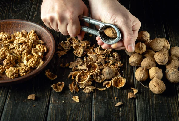 Peeling nuts from a hard shell by the hands of a cook using a nutcracker on the kitchen table. Preparation of nuts for use in cooking.