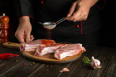 Şef ızgaradan önce çiğ ete kırmızı biber ekliyor. Mutfak masasında baharatlar ve baharatlarla çalışma ortamı