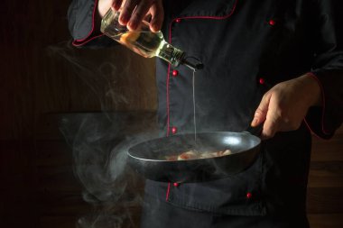 Şef kızartma tavasında kızarmış havuç ve soğana zeytinyağı ekler. Öğle yemeği için sebze pişiriyorum. Karanlık bir arkaplanda restoran ya da otel menüsü.