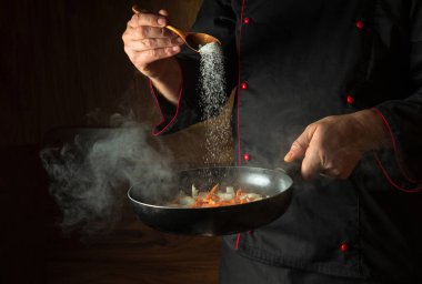 Aşçı sıcak tavaya tuz ekler. Akşam yemeği pişirmeden önce havuçla soğan kızartıyorum. Koyu arkaplanda tarif ya da menü için boşluk.