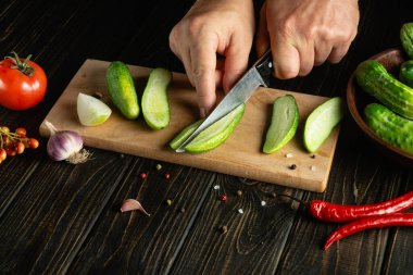 Şef baharat ve sebzeli salatalık turşusu için taze salatalık keser. Mutfak masasında çalışırken aşçıların ellerini yakın plan çek. Reklam için yer