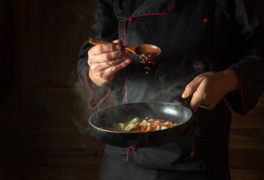 Şef kızartma tavasında kızarmış havuç ve soğana kuru biber ekler. Öğle yemeği için sebze pişiriyorum. Karanlık bir arkaplanda restoran ya da otel menüsü