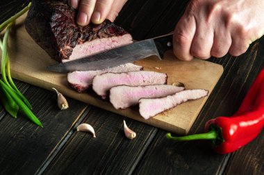 Sandviçler için mutfak tahtasının üzerinde füme et dilimliyorum. Elleri bıçaklı bir aşçının yakın çekimi. Fast street food fikri