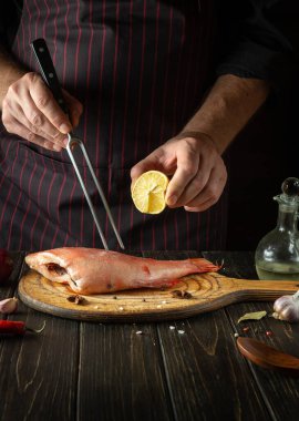 Şef pişirmeden önce Sebastes balığının üzerine limon suyu sıkıyor. Menü fikri ya da karanlık arka planda bir restoranın lezzetli tarifi..