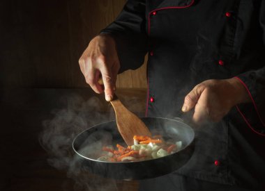 Bir aşçının elinde sıcak bir tavada sebze pişirmek. Tarif için karanlık arka planda yer var. Restoran veya otel menüsü
