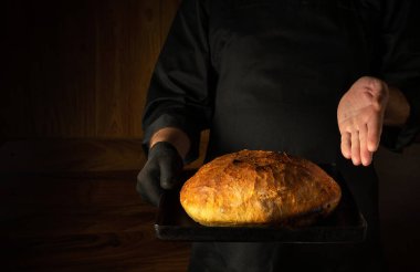 Aşçı ya da fırıncı elinde taze pişmiş buğday ekmeği ile bir çarşaf sunar. Menü veya tarif için boş karanlık boşluk.