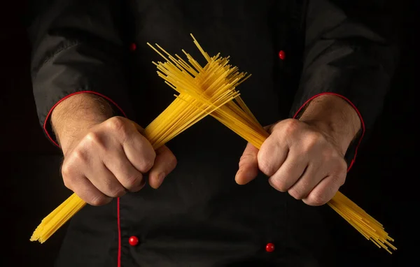 The chef breaks spaghetti with his hands in the kitchen. The concept of cooking the Italian national dish on a dark background.