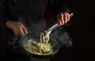 Profesyonel şef, haşlanmış tavada baharatlı ve baharatlı spagetti pişiriyor. Menü için bir restoran veya otel alanı