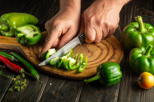 The cook cuts green pepper on a cutting board for making spicy adjika. Peasant delicious food. Copy space.