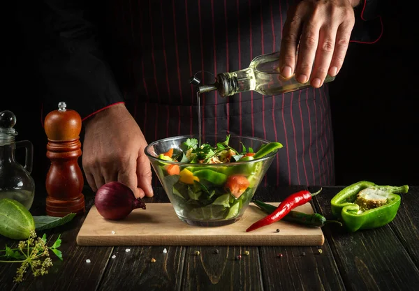 Experienced chef adds olive oil on a salad of fresh vegetables in a plate on a wooden board. Cooking healthy food in the kitchen with the hands of a cook