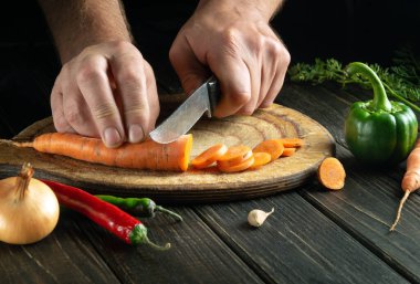 Şef, vejetaryen yemeği ya da yemeği hazırlamak için havucu kesme tahtasının üzerinde küçük parçalara ayırır. Mutfak masasında sebzeler var.