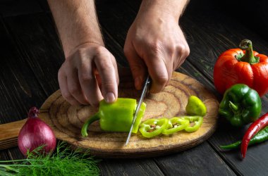 Şef elleri lezzetli yemekler hazırlamak için yeşil taze biberleri bir kesme tahtasına kesti. Vejetaryen menüsü ya da tarif fikri
