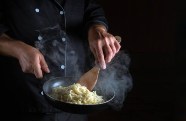 Profesyonel şef sıcak tavada spagetti kızartıyor. Siyah arkaplanda reklam alanı.
