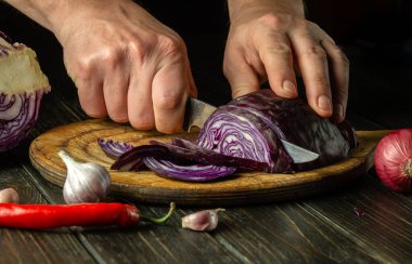 Şef salata için mutfak tahtasının üzerinde kırmızı lahana keser. Evde vejetaryen yemeği pişirmek.