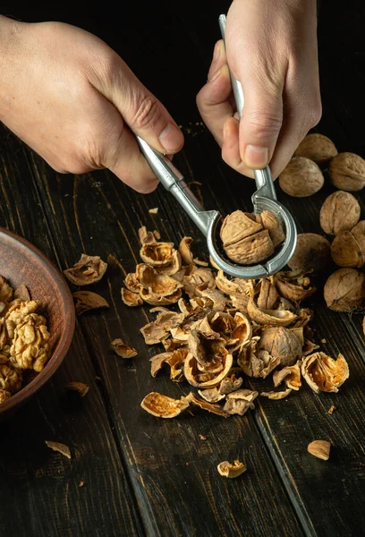 Peeling nuts from a hard shell by the hands of a cook using a nutcracker on the kitchen table. Preparation of nuts for use in cooking.