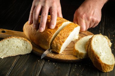 The hands of a chef with a knife cut fresh wheat bread before breakfast or lunch. The concept of traditional food or national dish. Copy space