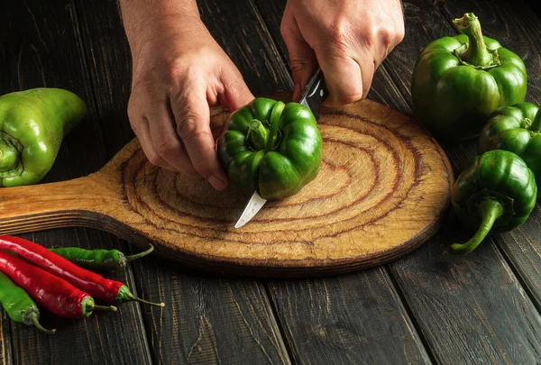 The cook hands with a knife cut fresh green peppers to prepare a delicious salad at home. Peasant food. Copy space